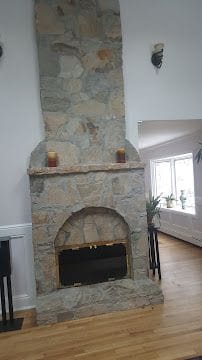 Floor-to-ceiling natural stone fireplace with wood mantel in a remodeled Connecticut living room