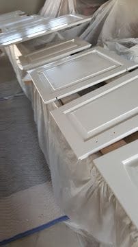 Freshly sprayed white cabinet doors drying on racks during a kitchen cabinet refinishing project in Connecticut